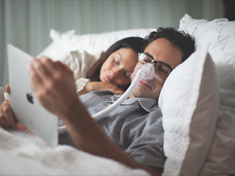 Image of a man using an iPad in bed with a woman laying next to him on Nemphos Braue's website