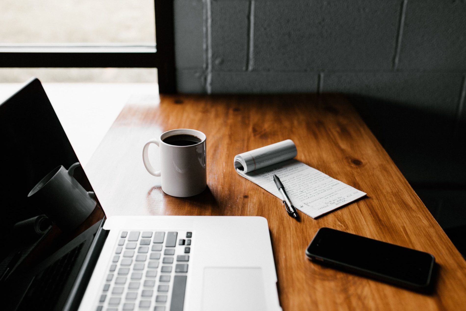 Image of a desk with a laptop, notepad, phone, and coffee cup on Nemphos Braue's website