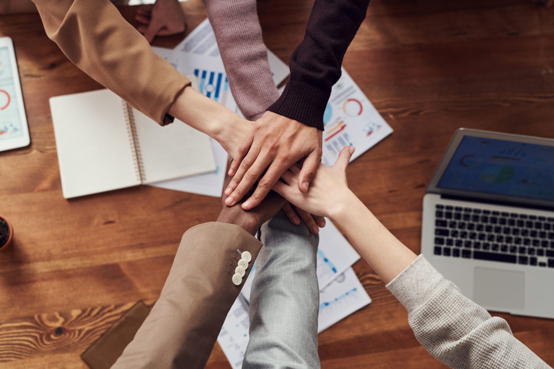 Image of people putting their hands together over a desk with papers and a laptop on Nemphos Braue's website