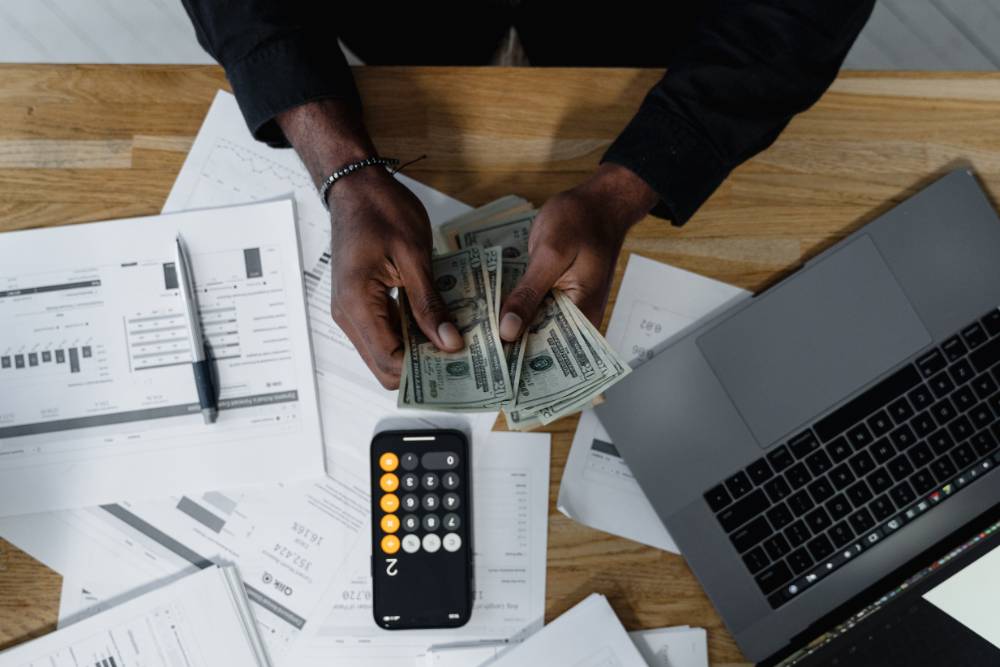 Image of a man counting cash at a desk with a laptop and various documents